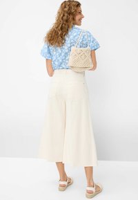 Chemise à manches courtes fleurie bleu clair, pantalon large crème, sac à main en toile texturé beige, et sandales espadrilles claires.