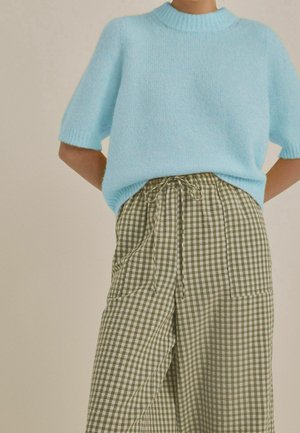 Jasnoniebieski krótki sweter dzianinowy z krótkim rękawem, zestawiony z wysokim stanem spodni w oliwkowo-białą kratkę, z wiązaniem w talii.