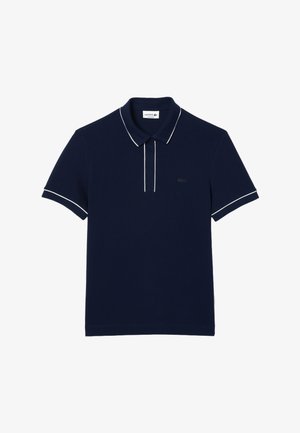 Granatowy polo z kołnierzykiem, białym obramowaniem na kołnierzyku i rękawach oraz małym haftowanym logo na piersi. Materiał bawełniany.