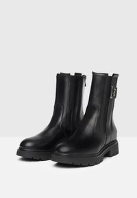 Schwarze Leder-Stiefeletten mit glatter Textur, seitlichen Reißverschlüssen und einer geschnallten Akzentuierung. Dicke Gummisohlen für Halt und Langlebigkeit.