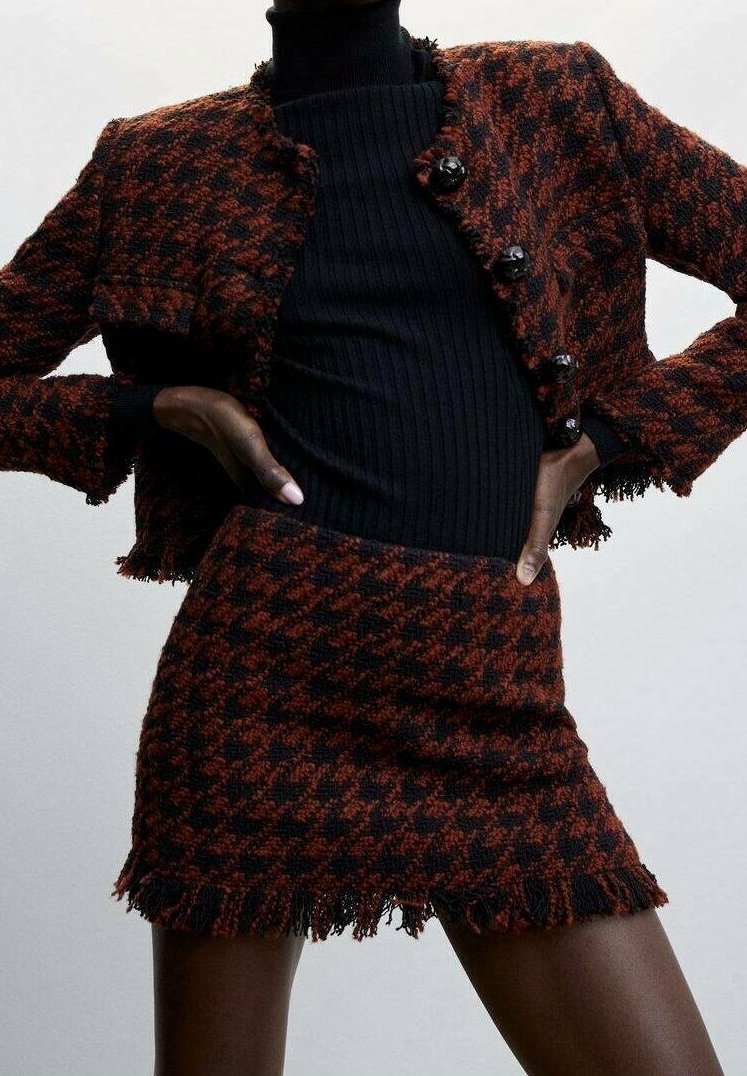 Veste en pied-de-poule tissée en orange et noir avec des bords frangés, assortie à un col roulé noir côtelé et une mini jupe assortie.