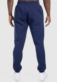 Marineblaue Schw sweatpants mit entspanntem Schnitt, elastischem Bund und Rippbündchen. Glatte Textur mit seitlichen Taschen. Kombiniert mit weißen Sneakers.