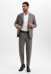Męski garnitur w szary wzór w jodełkę, z marynarką o usztywnionej konstrukcji i dopasowanymi spodniami, zestawiony z białą koszulą i czarnymi skórzanymi butami.