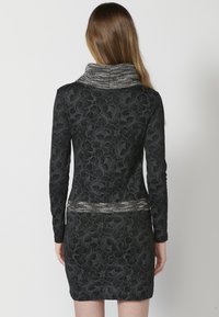 Schwarzes Kleid mit langen Ärmeln, floralem Muster und strukturiertem grauem Schalkragen. Betont eine taillierte Taille und hat einen kurzen Saum.