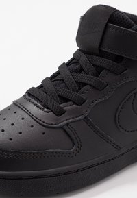 Svart lädersneaker med texturerad ovandel, perforerad tåbox, platta svarta snören och en logotypdetalj på den vadderade tungan. Slät gummisula.