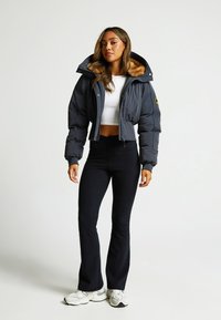 Giacca piumino corta blu navy con un grande cappuccio foderato in pelliccia sintetica, abbinata a leggings neri a zampa d'elefante e sneakers bianche.