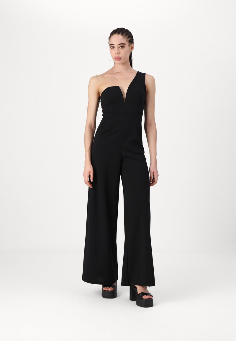 En-skapz svart jumpsuit med én skulder, dyp utringning, vide ben og en tettsittende overkropp. Laget av glatt stoff, kombinert med klumpete platåsko.