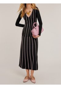 Musta neulepuku vaaleanpunaisilla pystysuorilla raidoilla, jossa on V-päällysteinen pitkähihaine paita ja siihen sopiva hame. Täydennetty vaaleanpunaisella käsilaukulla ja tasapohjaisilla kengillä.