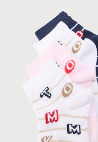 Στοίβα από τέσσερα πολύχρωμα καλτσάκια αστραγάλου με ρίγες και κεντημένα γράμματα και σχέδια ποδοσφαίρου σε λευκό φόντο.