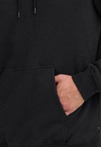 Zwarte sweatshirt met een voorkrui pocket, trekkoordkapuchon en geribde manchetten. De stof lijkt zacht en heeft een iets gestructureerde uitstraling.