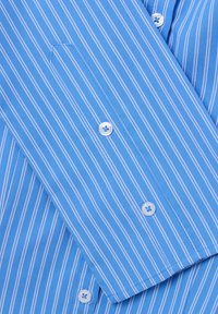 Camicia a righe blu chiaro con strisce bianche, dotata di una chiusura frontale con bottoni, una tasca sul petto con un lembo diagonale e bottoni bianchi standard.