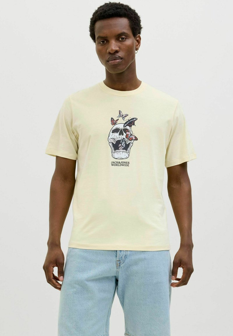 Sárga pamut póló koponya grafikával, pillangókkal és "JACK & JONES WORLDWIDE" felirattal, rövid ujjú és kerek nyakkivágással.