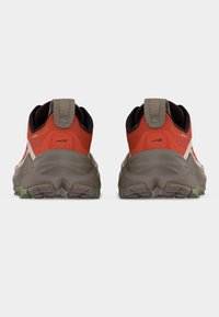 Ζεύγος κόκκινων και μπεζ παπουτσιών για τρέξιμο σε μονοπάτι με παχιά γκρι σόλα και πράσινη χάραξη, εμφανιζόμενα από πίσω σε λευκό φόντο.