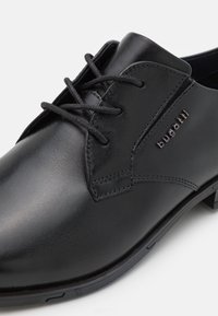 Schwarze Leder-Schuh mit runder Zehenpartie, flachen Schnürsenkeln und geprägtem Branding. Glatte Oberfläche mit minimalen Nähten.