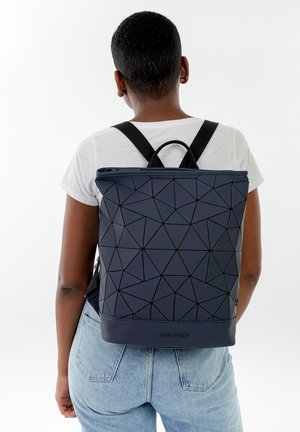 Sac à dos bleu marine à motif géométrique avec une surface texturée et des accents noirs, doté de bretelles et d'une poignée supérieure pour le transport.