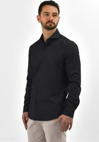 Zwarte overhemd met een slank ontwerp, lange mouwen en een puntige kraag. Gemaakt van zachte stof, met een getailleerde silhouette en subtiele textuur.