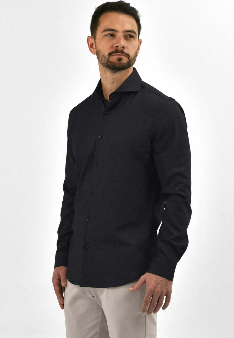 Zwarte overhemd met een slank ontwerp, lange mouwen en een puntige kraag. Gemaakt van zachte stof, met een getailleerde silhouette en subtiele textuur.