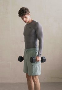 Pilka ilgomis rankovėmis sportinė marškinėliai, derinami su šviesiai žaliais šortais. Asmuo laiko juodus hantelius. Lygus tekstūra ir prigludusi forma.