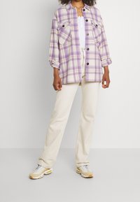 Rutigt skjorta i ljuslila och beige med två framfickor, kombinerat med krämfärgade vida byxor och beige sneakers med reflexdetaljer.