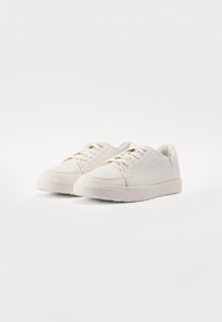 Sapatilhas brancas de couro com forma arredondada, superfície texturizada e sola de borracha plana. Apresentam atacadores planos e um design minimalista.