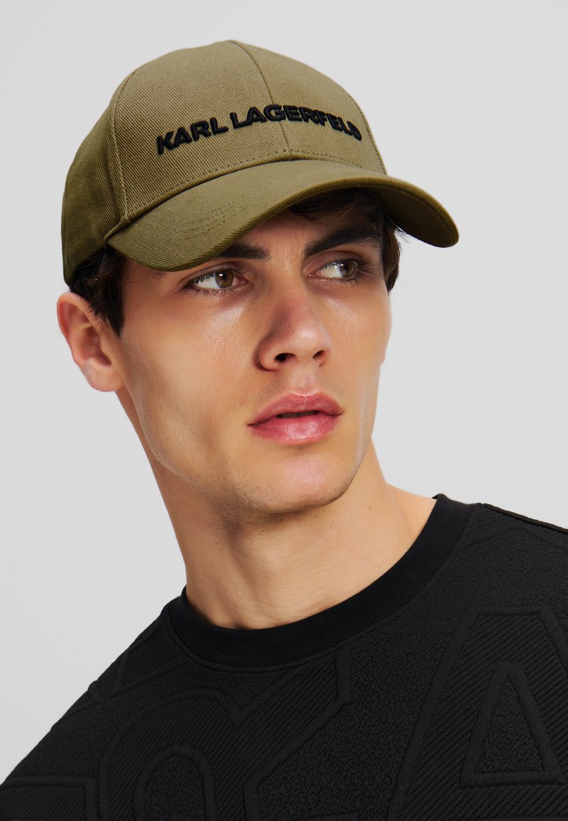 Olijfgroene baseballpet met "KARL LAGERFELD" geborduurd in het zwart. Heeft een gestructureerde klep en een textuurpatroon.