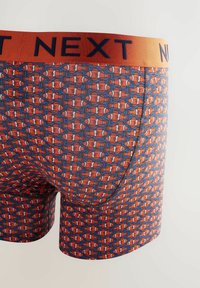 Herren-Boxershorts mit einem blauen und orangefarbenen Fischmuster, ausgestattet mit einem weichen elastischen Bund, auf dem "NEXT" in Marineblau gedruckt ist. Dehnbares, bequemes Material.