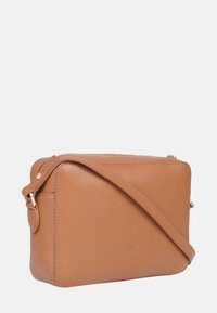 Prostokątna brązowa torebka na ramię z regulowanym paskiem, subtelnym wytłoczonym logo i ziarnistą fakturą na jednolitym tle.