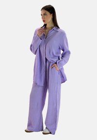 Conjunto de dos piezas morado hecho de un tejido texturizado, que incluye una camisa de manga larga con botones y pantalones de pierna ancha y holgados.