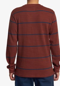 Langärmliges Shirt in rotbraun, mit strukturiertem Waffelgewebe und blauen horizontalen Streifen über den Rücken. Standard Rundhalsausschnitt.