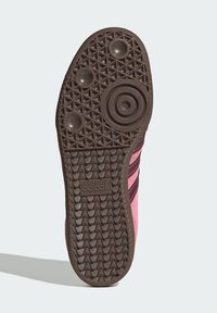 Braune Gummisohle mit kreisförmigem und diamantförmigem Muster, ausgestattet mit einem pinkfarbenen Obermaterial mit schwarzen Streifen und einem geprägten Logo an der Ferse.