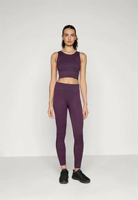 Vijolična športna kratka majica in ujemajoče visoko pasne legice, izdelane iz elastičnega materiala, z gladko teksturo, minimalnimi šivi in prilegajočim dizajnom.