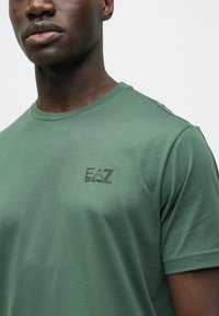 Zöld rövid ujjú póló puha pamut keverék anyagból, kerek nyakkivágással és fekete EA7 Emporio Armani logóval a bal mellrészen.