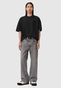 Camiseta negra de gran tamaño, jeans grises de corte holgado, cinturón negro, zapatillas beige con suelas negras, con branding minimalista en la camiseta.