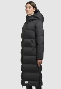 Schwarze Daunenjacke mit einem langen, taillierten Design, gestepptem Muster, vollem Kapuzen und einer seitlichen Reißverschlusstasche. Die Vorderseite hat einen Reißverschluss.