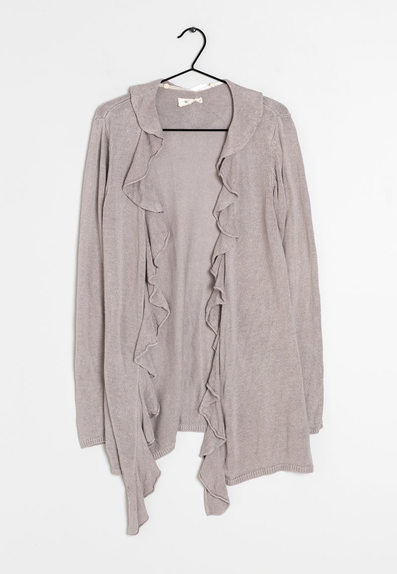 Vaaleanharmaa neuletakki, joka on valmistettu teksturoidusta neulosmateriaalista ja jossa on röyhelötrimmi etureunoilla ja kaula-aukossa. Ripustettuna mustasta koukusta.