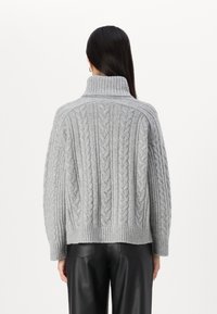 Pull en maille grise avec col montant, arborant des motifs complexes et des détails texturés. Le design comprend des manches longues et une coupe décontractée.