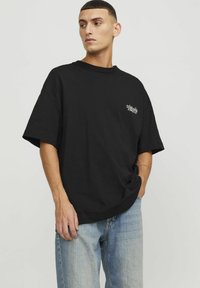 T-shirt nera oversize in cotone, con una piccola stampa del logo bianco sul lato sinistro del petto, scollatura rotonda e maniche corte.