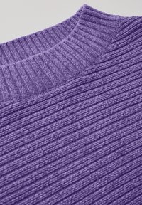 Gros plan sur un pull violet à côtes, présentant une surface texturée et un col rond. Le tissu affiche un fini doux et duveteux.