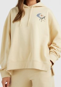 Felpa oversized beige realizzata in tessuto morbido, con un design grafico sul petto sinistro e stringhe sul cappuccio.