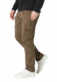 Cargo-Hosen aus braunem Baumwollstoff, mit mehreren Seitentaschen, lockerer Passform und kombiniert mit weißen Sneakers.