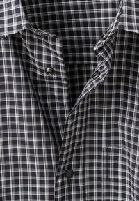 Camisa a cuadros en blanco y negro, confeccionada con una suave tela de algodón, con cuello puntiagudo, botones en la parte delantera y un bolsillo en el pecho.