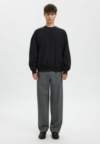 Czarna oversize bluza z okrągłym dekoltem, zestawiona z jasnoszarymi plisowanymi spodniami i czarnymi butami oxford, na białym tle.