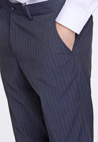 Mörkblå rutiga byxor i strukturerad tyg, med en slitsfick och en knappknäppning i midjan.