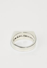 Bague en argent avec un dessus plat et des bords arrondis, comportant un texte gravé à l'intérieur. Surface métallique lisse, design minimaliste.