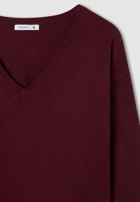 Maglione a V in tessuto a maglia color bordeaux scuro. Presenta scollatura e polsini a costine, con vestibilità comoda e maniche lunghe. Tag di taglia S visibile.