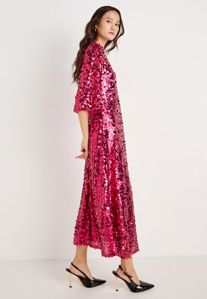 Pink sequin dress with a loose, mid-length design, featuring short sleeves and a rounded neckline. Worn with black heels.