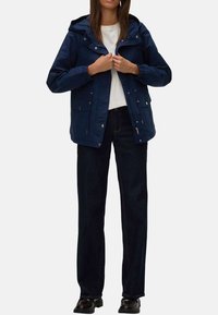 Veste imperméable bleu marine avec capuche, fermeture �éclair à l'avant et cordons réglables. Dispose de deux poches avant et d'une coupe décontractée.