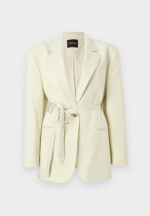 Kremfarget skreddersydd blazer med hakket slag, enkelt knappelukking, sidelommer og et stoffbelte knyttet i livet.