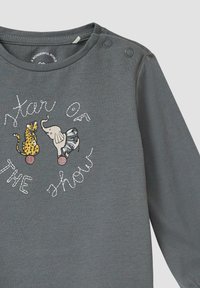 Grijze longsleeve shirt met ronde halslijn, voorzien van kleurrijke dierenprints en de tekst "Ster van de Show" in speelse stiksel. Drukknopen op de schouder.