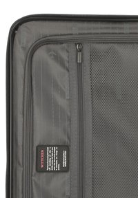 Interior de maleta gris con múltiples compartimentos con cremallera, panel de malla y etiqueta de marca. Presenta costuras verticales y una superficie texturizada.
